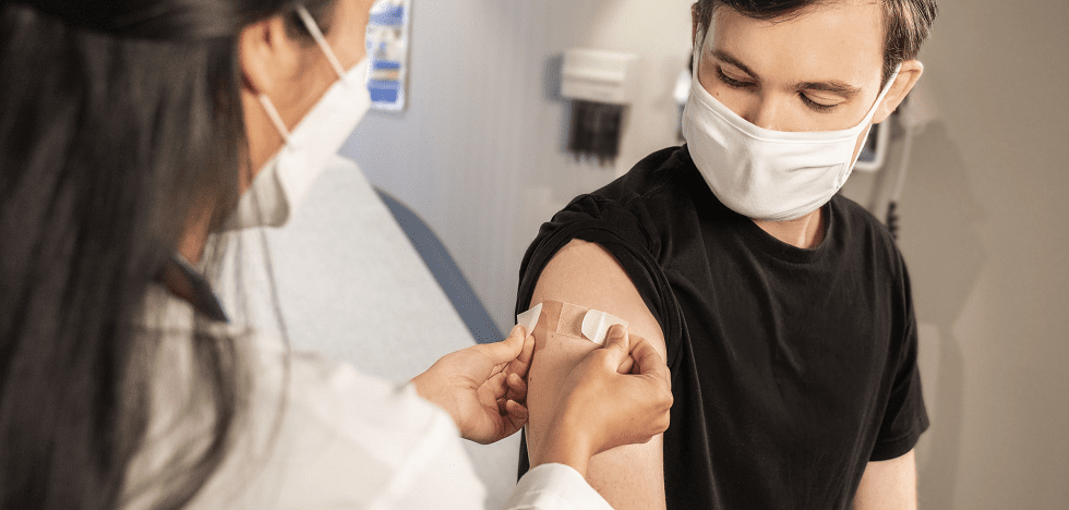 Eine Ärztin klebt einem Patienten nach seiner Impfung ein Pflaster auf den Arm